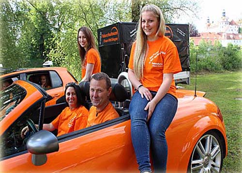 Teammitglieder im orangen Cabrio vor dem Fahrschul-Lkw