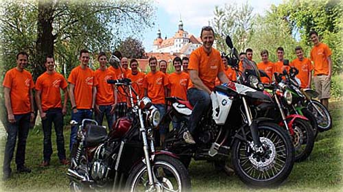 Das Fahrschulteam in orangen Shirts mit Motorrädern vor dem Neuburger Schloss
